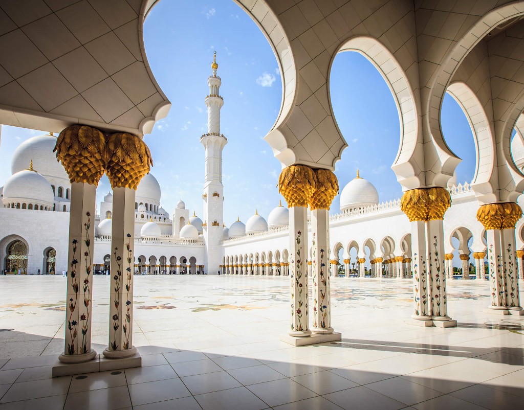 Sheikh Zayed Grand Mosque ornate marble columns and arches opening onto the sunlit courtyard with domes and minaret